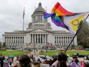 A supporter of trans rights waves a flag in front of the Temple of Justice as an opposing rally for opponents of legislation to exempt youth shelters from contacting parents of kids seeking gender-affirming health care gathers on the steps of the Capitol Building on April 21, 2023, in Olympia, Washington.