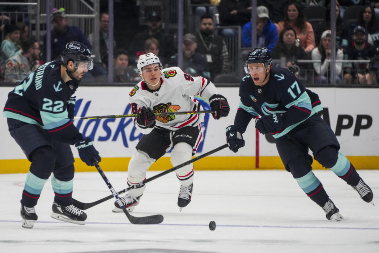 Seattle Kraken right wing Oliver Bjorkstrand (22) and center Jaden Schwartz (17) close in to take possession against Chicago Blackhawks center Connor Bedard, center, during the third period of an NHL hockey game Thursday, Nov. 14, 2024, in Seattle.