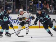 Seattle Kraken right wing Oliver Bjorkstrand (22) and center Jaden Schwartz (17) close in to take possession against Chicago Blackhawks center Connor Bedard, center, during the third period of an NHL hockey game Thursday, Nov. 14, 2024, in Seattle.