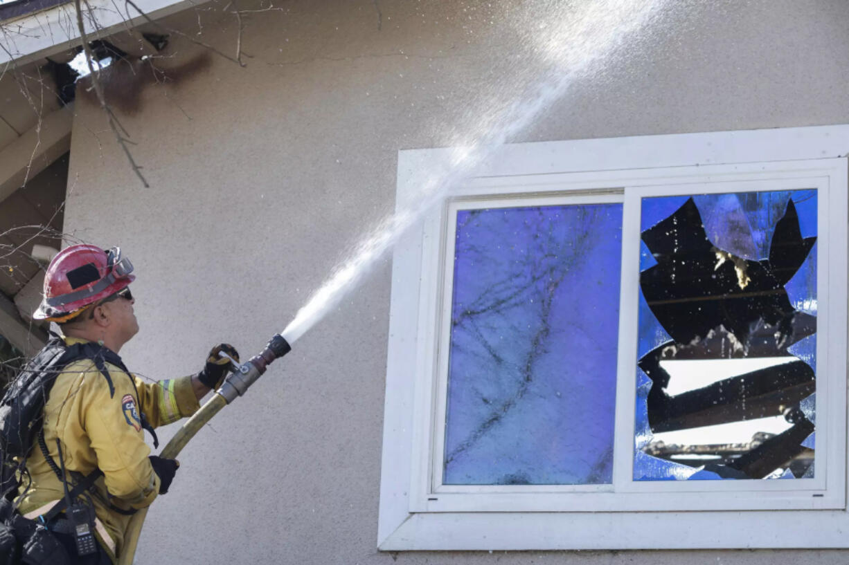 A firefighter douses a hotspot in the eaves of a home on Old Coach Drive in Camarillo. (Myung J.