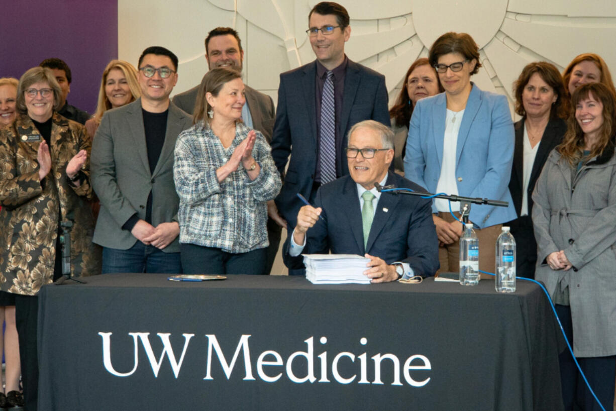 Washington Gov. Jay Inslee (seated) prepares to sign the 2024 supplemental budget on March 29, 2024. He was joined by several Democratic state lawmakers, including, to his right, Sen. June Robinson, the lead Senate budget writer.