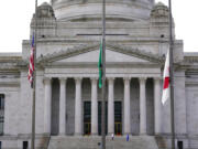 A person poses for photos as flags fly at half-staff in front of the Legislative Building at the Capitol in Olympia, Wash., Wednesday, May 25, 2022. (AP Photo/Ted S.