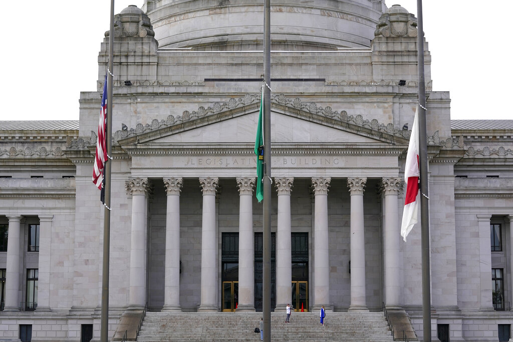 A person poses for photos as flags fly at half-staff in front of the Legislative Building at the Capitol in Olympia, Wash., Wednesday, May 25, 2022. (AP Photo/Ted S.