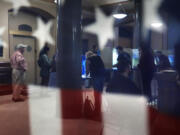 Voters are reflected in a window near an American flag as they mark their ballots during early voting in the general election, Friday, Nov. 1, 2024, at City Hall in Providence, R.I.