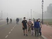 A foreign tourist family walks wearing face mask amidst a thick layer of smog as air pollution shoots up in New Delhi, India, Monday, Nov. 18, 2024.