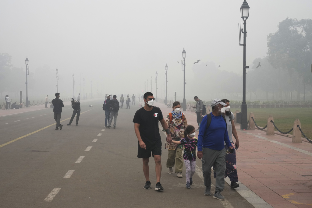 A foreign tourist family walks wearing face mask amidst a thick layer of smog as air pollution shoots up in New Delhi, India, Monday, Nov. 18, 2024.