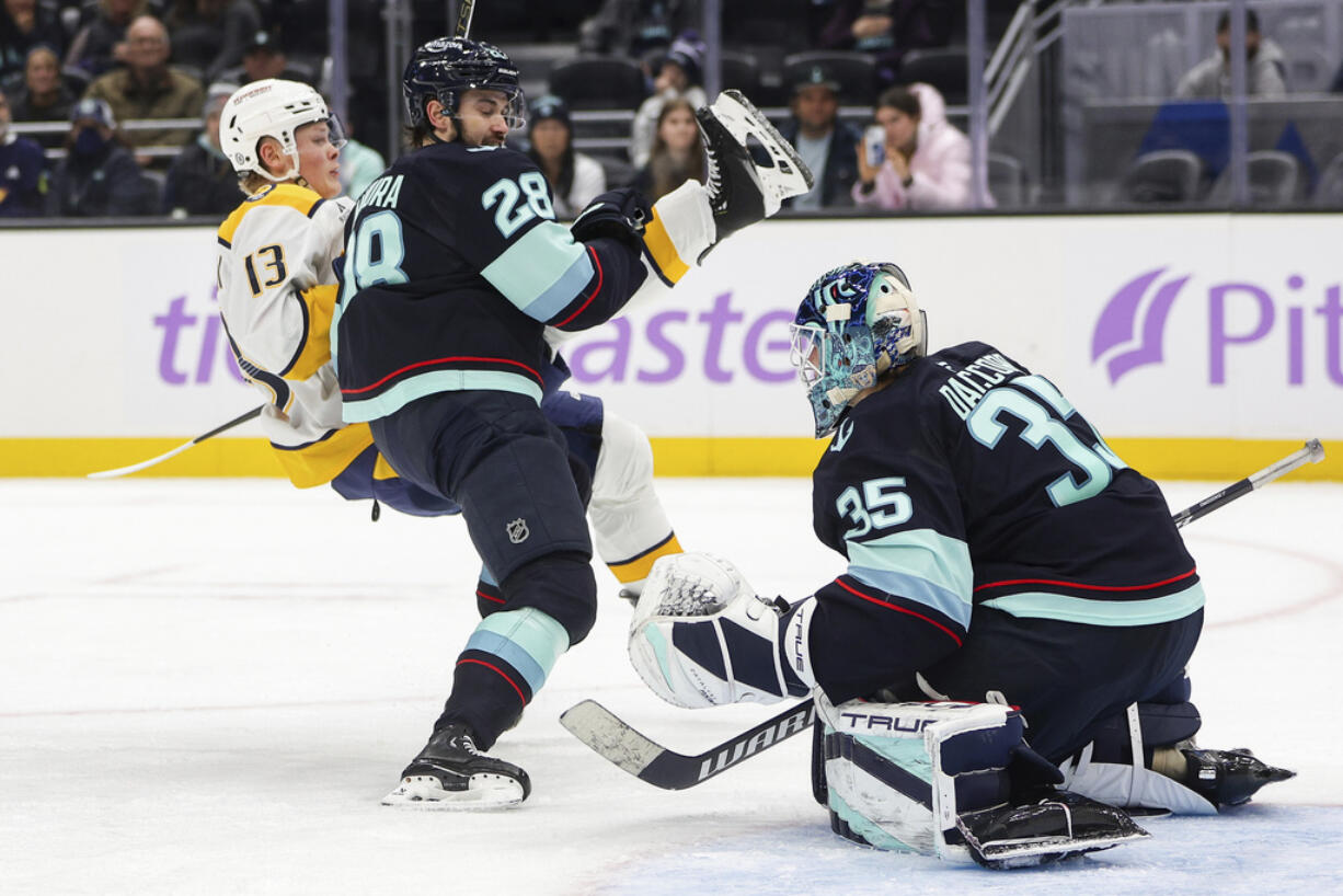 Nashville Predators center Juuso Parssinen (13) is hit by Seattle Kraken defenseman Joshua Mahura (28) in front of the goal during the second period of an NHL hockey game, Wednesday, Nov. 20, 2024, in Seattle.