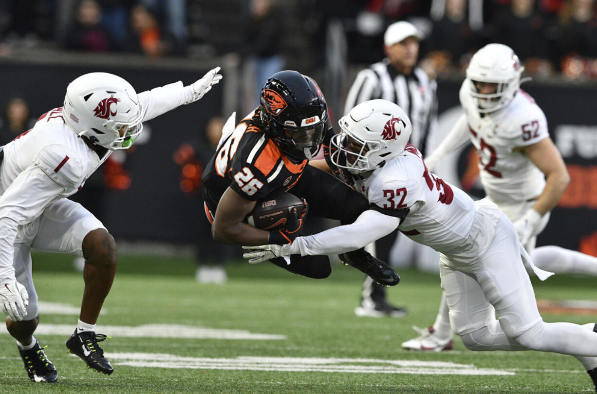 Washington State defensive backs Stephen Hall (1) and Tanner Moku (32) tackle Oregon State running back Salahadin Allah (26) during the first half of an NCAA college football game Saturday, Nov. 23, 2024, in Corvallis, Ore.