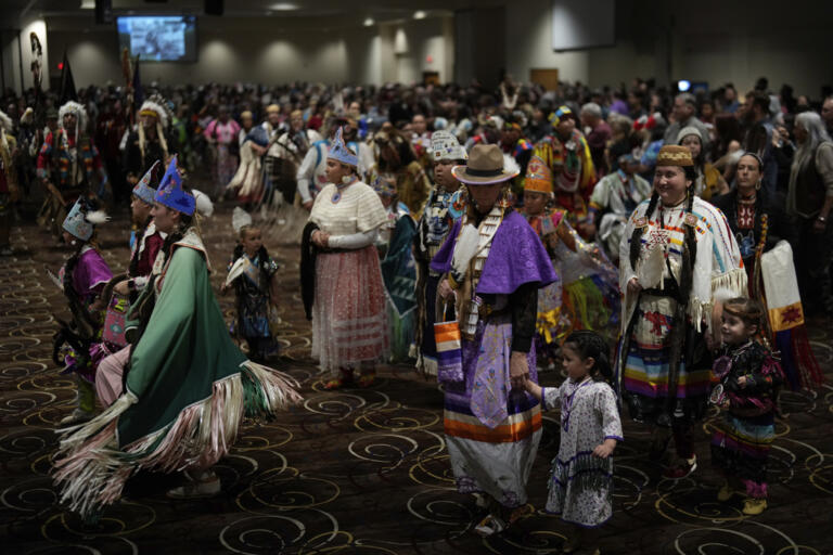 Tiffany Stuart, at right in white, holds hands with her daughter Kwestaani Chuski Stuart, bottom right, as they participate in a powwow at Chinook Winds Casino Resort, Saturday, Nov. 16, 2024, in Lincoln City, Ore.