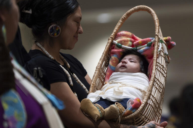 Kimberly Jurado holds her daughter, Delia Rubi Jurado, as they walk during a dance at a powwow at Chinook Winds Casino Resort, Saturday, Nov. 16, 2024, in Lincoln City, Ore.