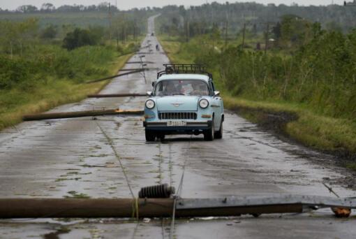 People drive along a road littered with fallen power lines after the passing of Hurricane Rafael in San Antonio de los Banos, Cuba, Thursday, Nov. 7, 2024.