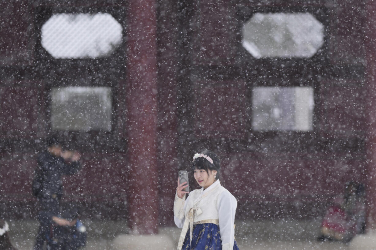 Chan Yian from Taiwan holds her smartphone in snow at the Gyeongbok Palace, one of South Korea&rsquo;s well-known landmarks, in Seoul, South Korea, Wednesday, Nov. 27, 2024.