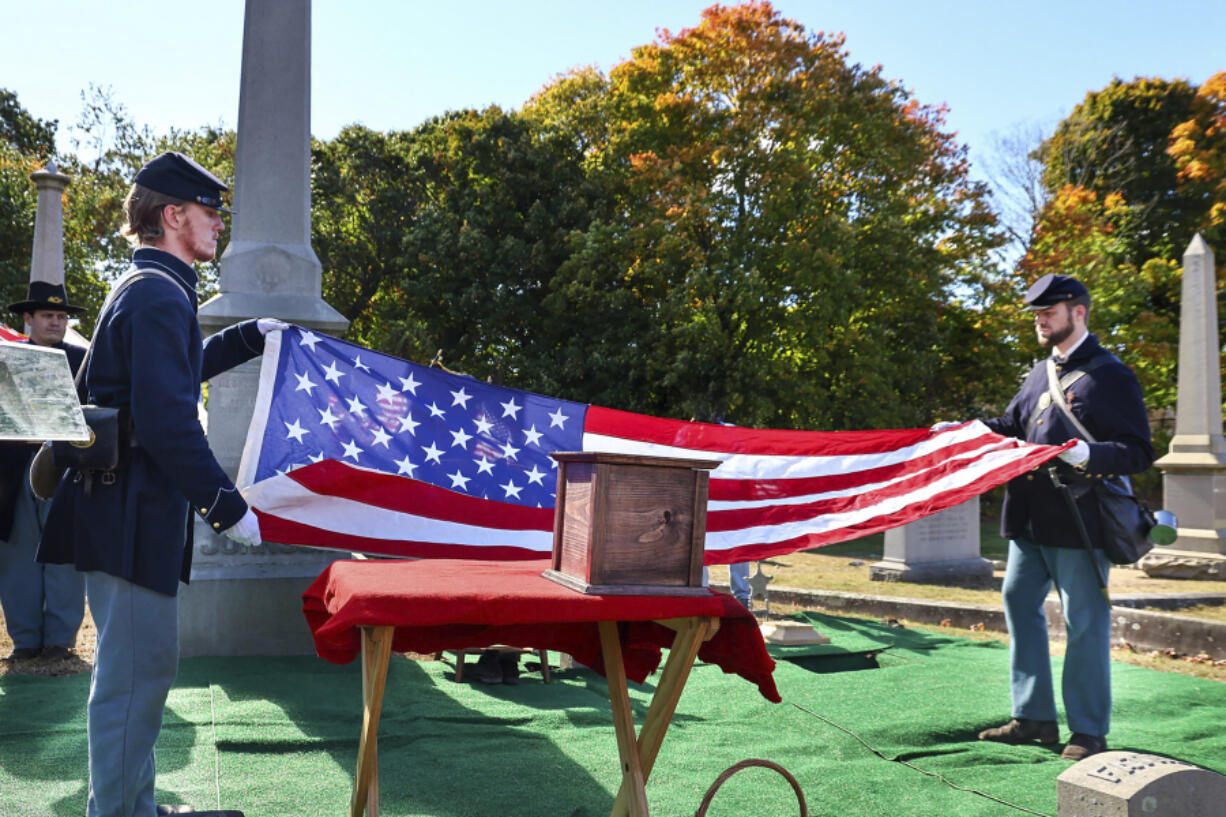 In this photo provided by The Valley Breeze, Civil War re-enactors fold an American flag near an urn, center, containing the cremated remains of Byron R. Johnson, a Union soldier who was born in Pawtucket, R.I., in 1844 and fought in the Civil War, during funeral services, Wednesday, Oct. 16, 2024, at Oak Grove Cemetery, in Pawtucket, after his remains were transferred from storage at a cemetery in Seattle.