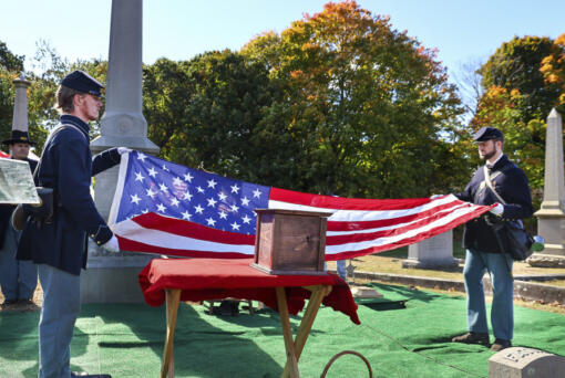 In this photo provided by The Valley Breeze, Civil War re-enactors fold an American flag near an urn, center, containing the cremated remains of Byron R. Johnson, a Union soldier who was born in Pawtucket, R.I., in 1844 and fought in the Civil War, during funeral services, Wednesday, Oct. 16, 2024, at Oak Grove Cemetery, in Pawtucket, after his remains were transferred from storage at a cemetery in Seattle.