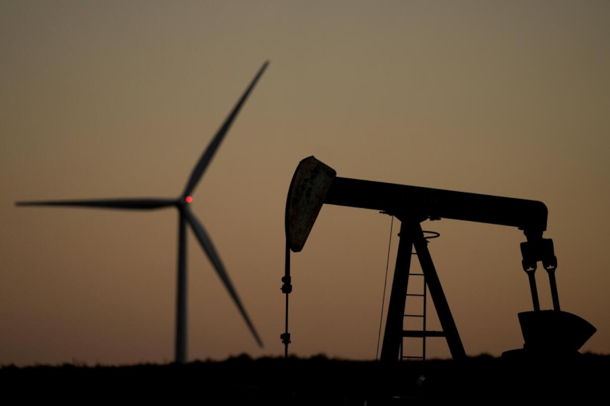 A pumpjack operates in the foreground while a wind turbine at the Buckeye Wind Energy wind farm rises in the distance, Monday, Sept. 30, 2024, near Hays, Kan.