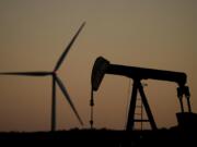 A pumpjack operates in the foreground while a wind turbine at the Buckeye Wind Energy wind farm rises in the distance, Monday, Sept. 30, 2024, near Hays, Kan.