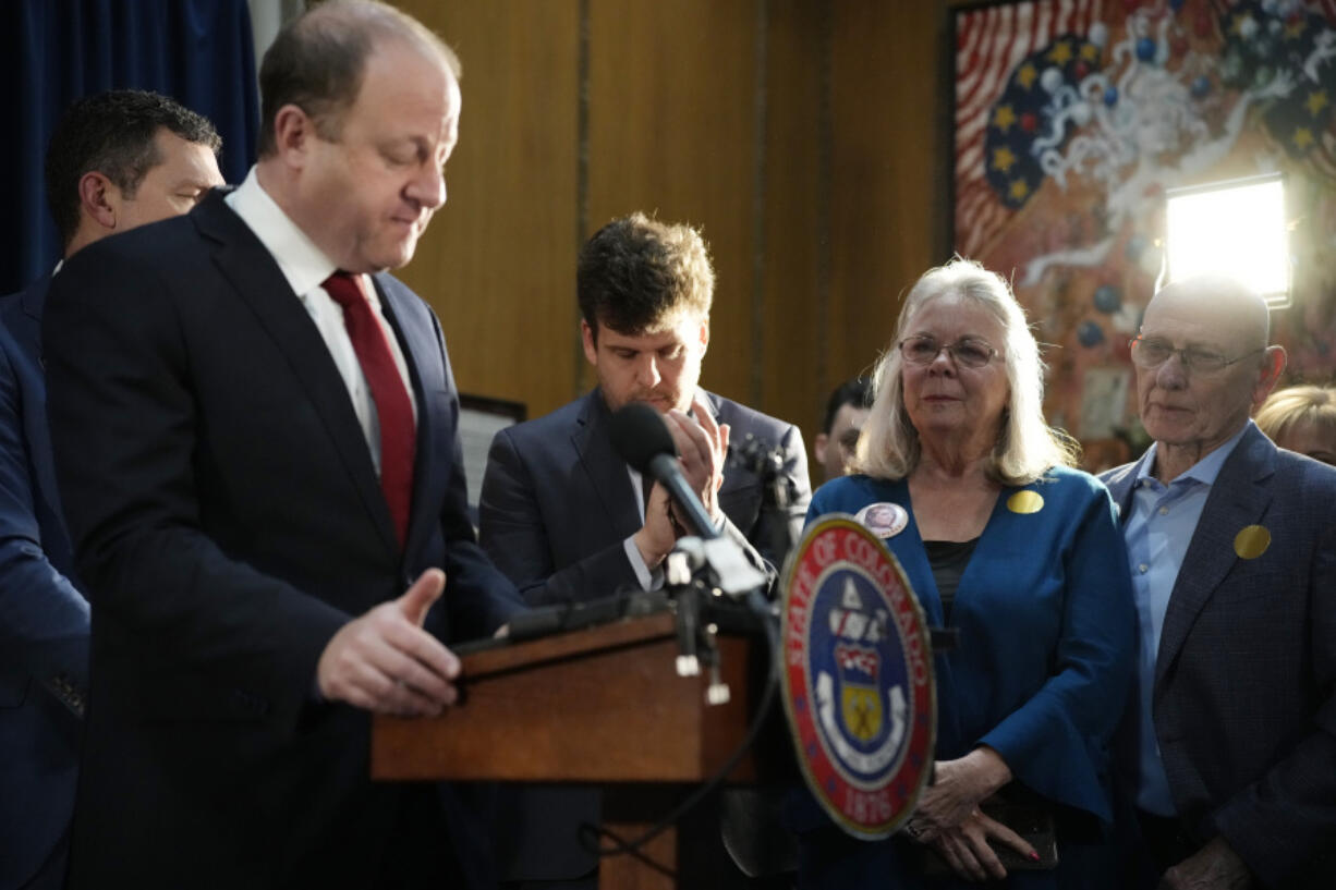 FILE - Colorado Gov. Jared Polis, front left, pauses as he speaks as Sandy Phillips, second from right, and her husband, Lonnie, who lost their daughter in the mass shooting at a theatre in Aurora, Colo., look on before Polis signed four gun control bills into law during a ceremony April 28, 2023, in the State Capitol in Denver.