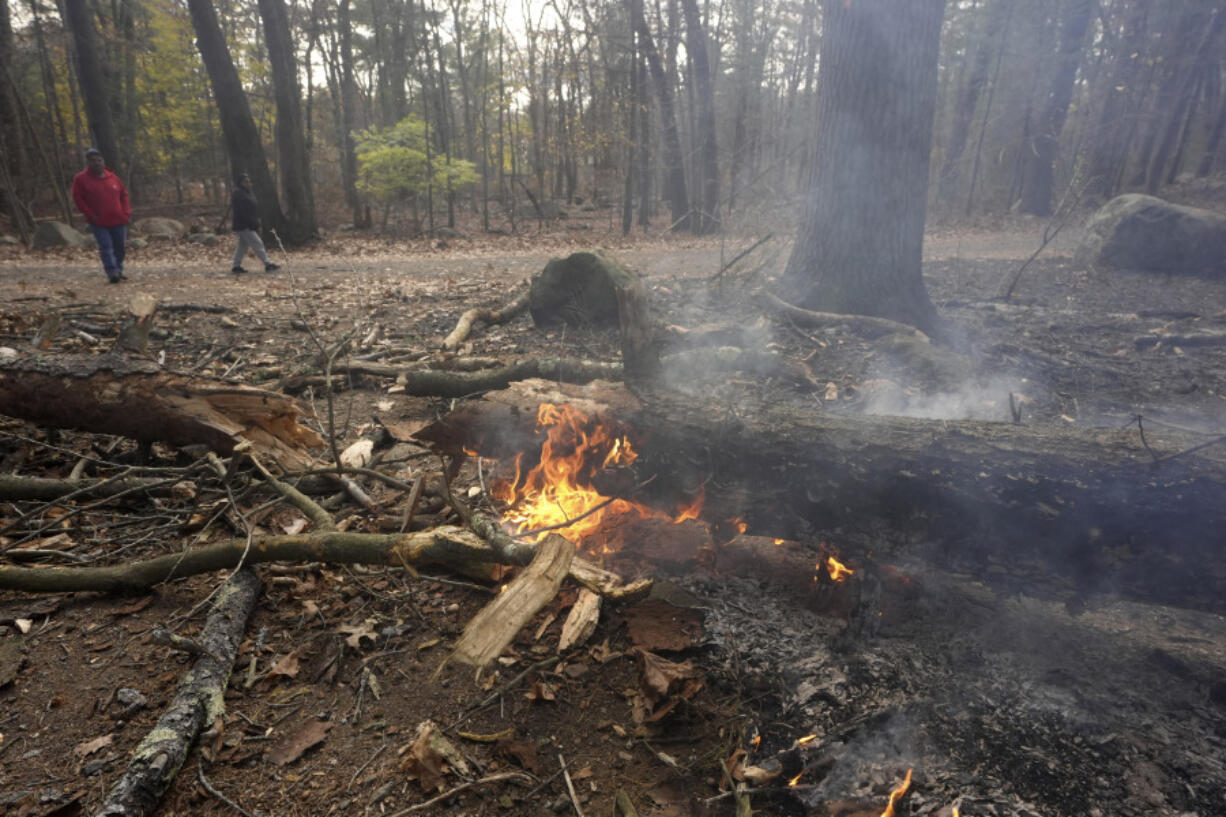 People walk along a path near flames on the forest floor, in Lynn Woods Reservation, Sunday, in Lynn, Mass.