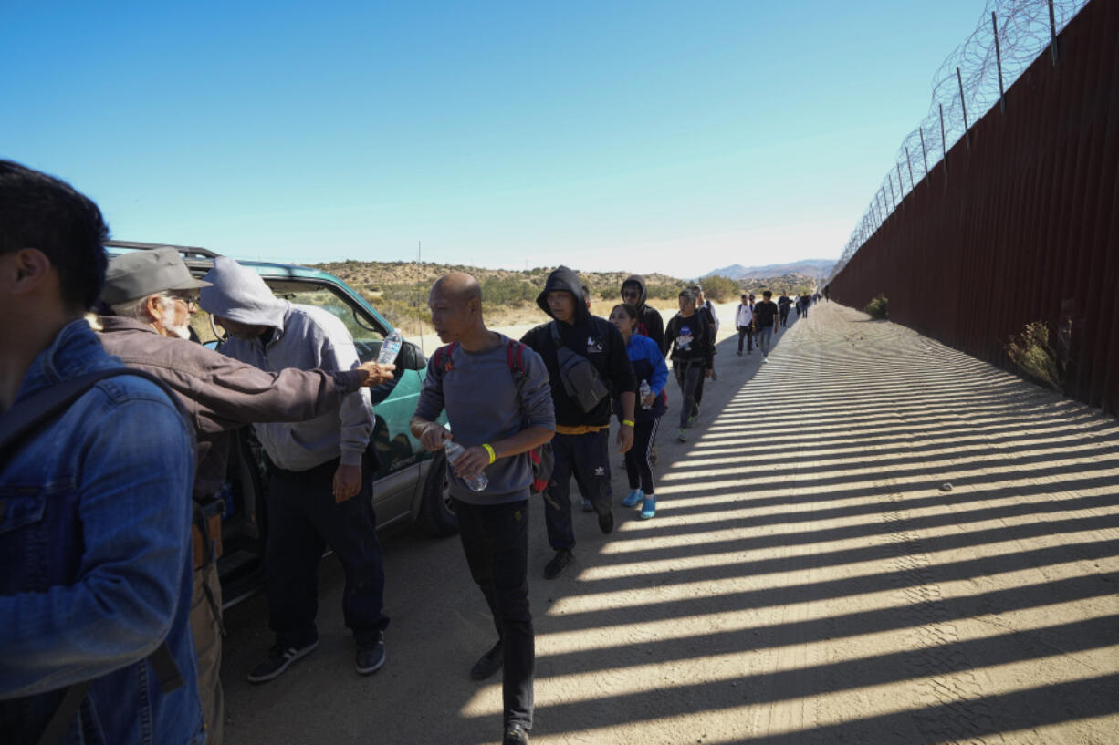 FILE - Sam Schultz, second from left, hands out water bottles to a line of asylum-seeking migrants, Tuesday, on Oct. 24, 2023, near Jacumba Hot Springs, Calif.