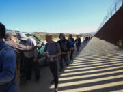 FILE - Sam Schultz, second from left, hands out water bottles to a line of asylum-seeking migrants, Tuesday, on Oct. 24, 2023, near Jacumba Hot Springs, Calif.