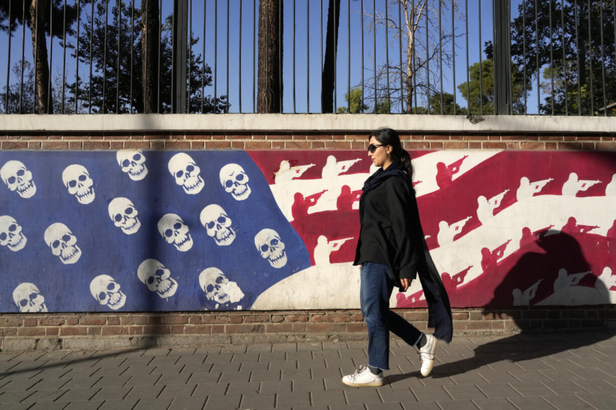 An Iranian woman walks past a satirised image of the U.S. flag on the wall of former U.S. embassy, in Tehran, Iran, Tuesday, Oct. 22, 2024.