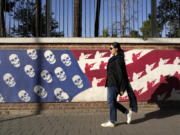 An Iranian woman walks past a satirised image of the U.S. flag on the wall of former U.S. embassy, in Tehran, Iran, Tuesday, Oct. 22, 2024.