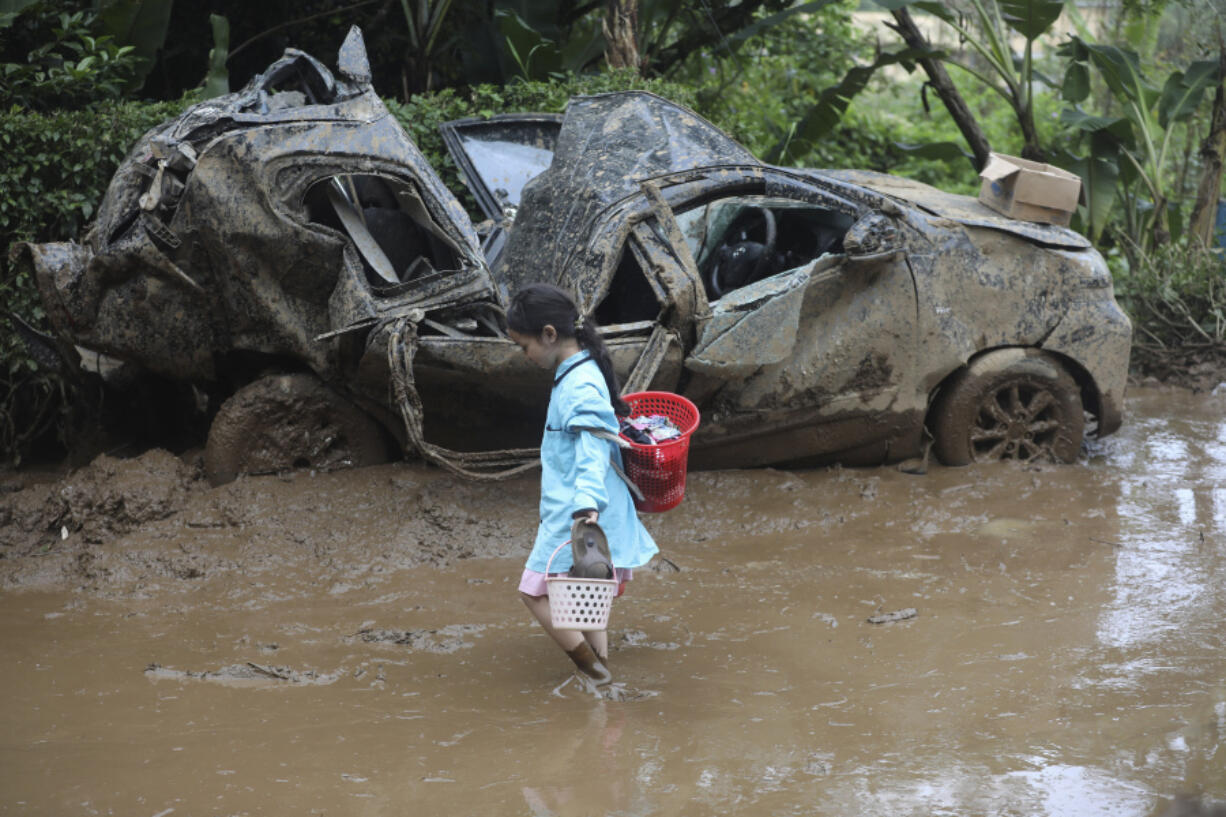 A young girl walks past the wreckage of a car after a landslide killed a number of people and left some others missing in Karo, North Sumatra, Indonesia, Monday, Nov. 25, 2024.