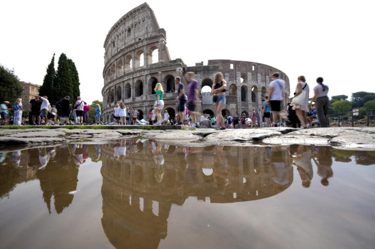 FILE - Tourists walk by the ancient Roman Colosseum as it&rsquo;s reflected in a puddle, in Rome, Sept. 5, 2024.