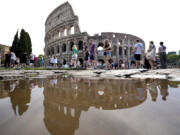 FILE - Tourists walk by the ancient Roman Colosseum as it&rsquo;s reflected in a puddle, in Rome, Sept. 5, 2024.