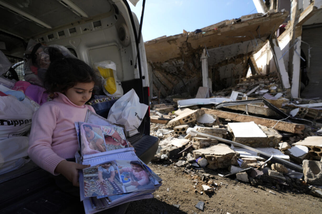 Yara Srour, 4, holds her photo album, as she sits in front of her grandparents destroyed house after she returned with her family to Hanouiyeh village, southern Lebanon, Thursday, Nov.