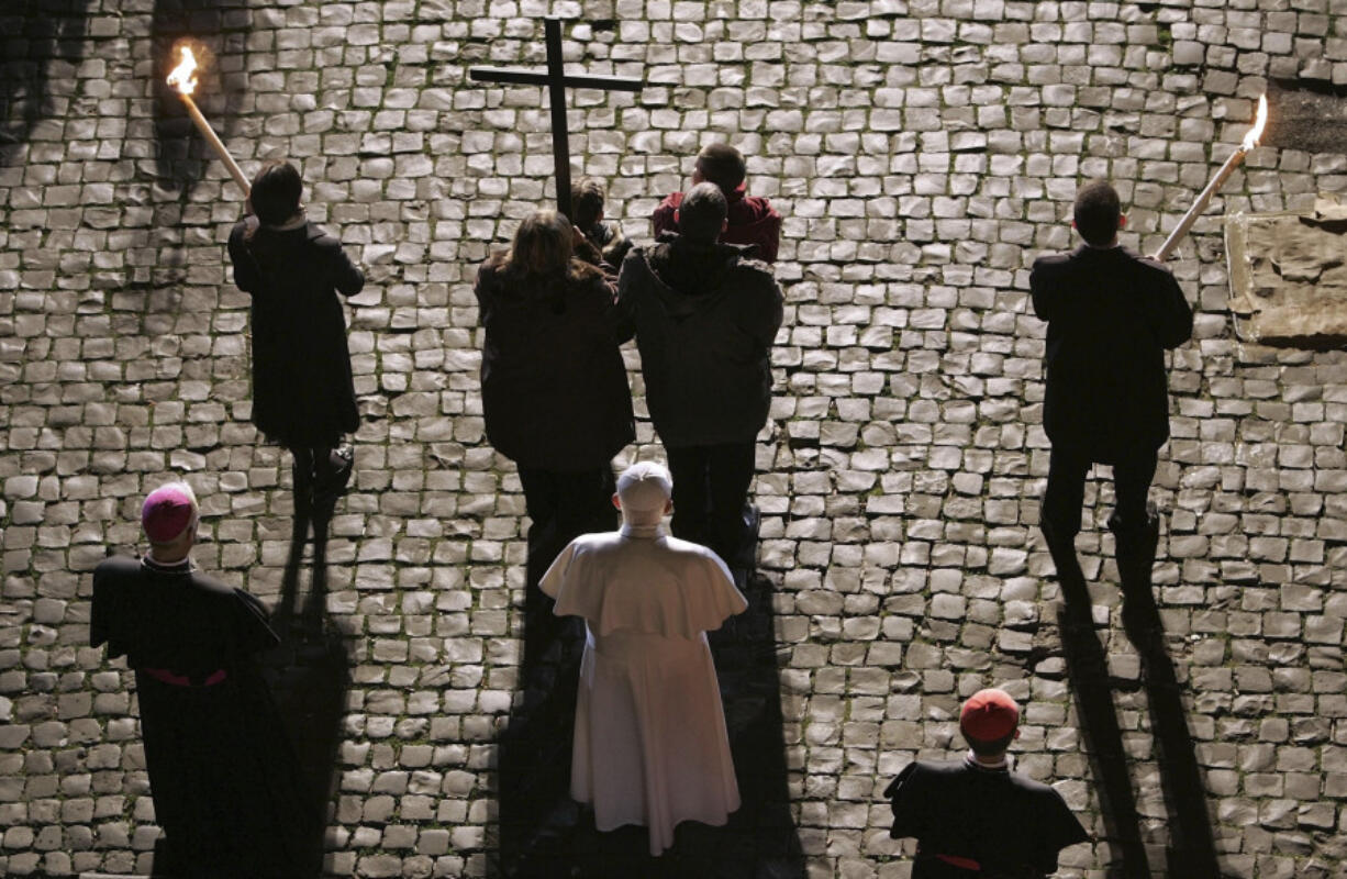 FILE - Pope Benedict XVI, in white at center, stands still on the cobblestone pavement behind a family carrying a wooden cross, during the Via Crucis (Way of the Cross) torchlight procession celebrated by the pontiff on Good Friday at the ancient Colosseum in Rome, April 6, 2007.