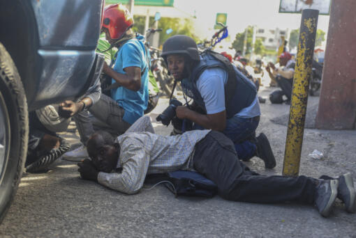 Journalists take cover from the exchange of gunfire between gangs and police in Port-au-Prince, Haiti, Monday, Nov. 11, 2024.