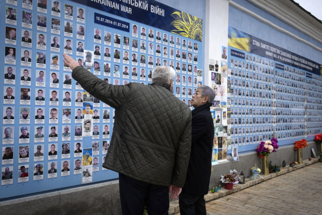 Japanese Foreign Minister Takeshi Iwaya, right, and Ukrainian Foreign Minister Andriiy Sybiha look at photos of fallen soldiers Saturday after a flower-laying ceremony at a memorial wall in Kyiv, Ukraine.