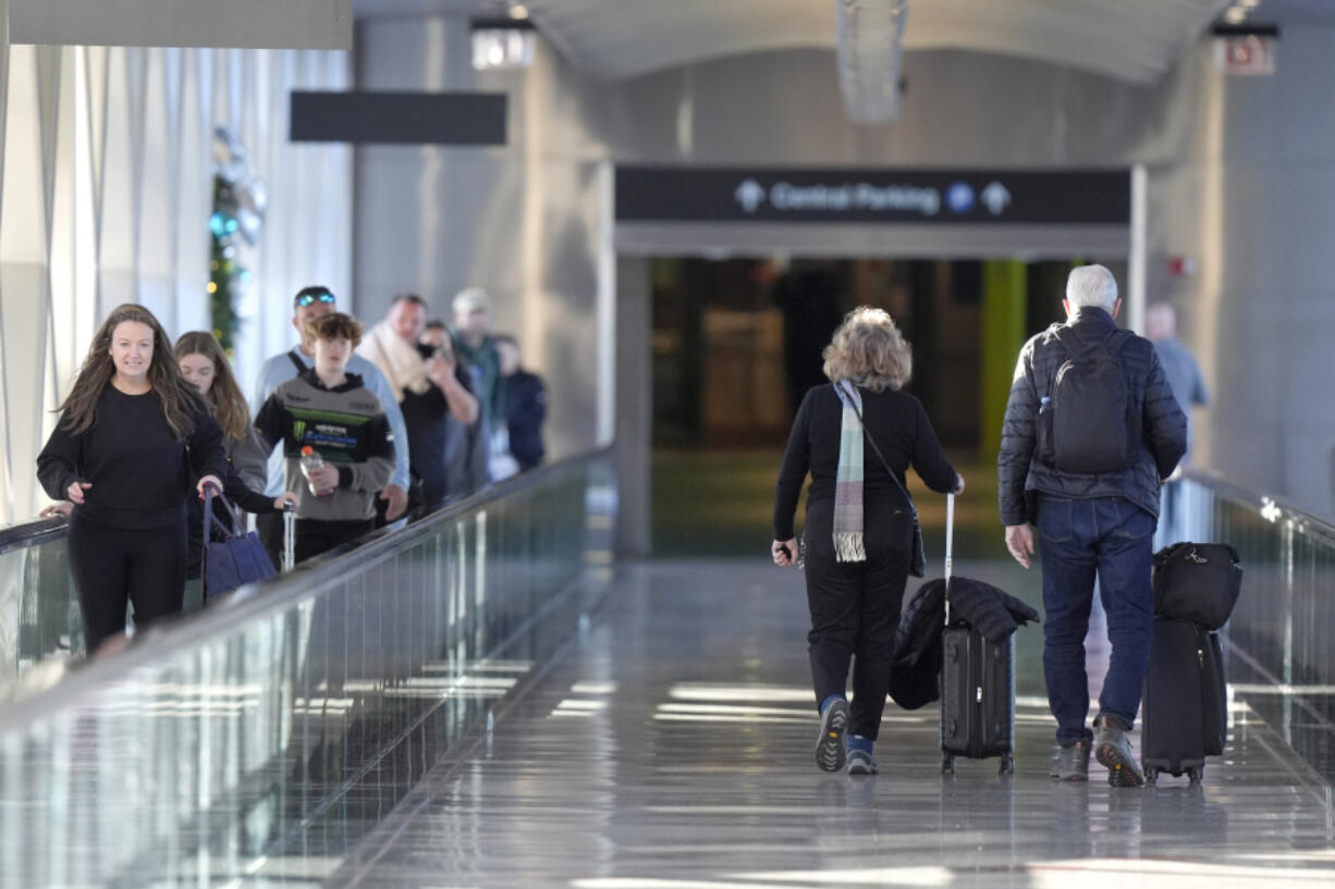 Travelers use a moving walkway, left, and pull suitcases, right, in an airport terminal, Monday, Nov. 25, 2024, at Boston Logan International Airport, in Boston.