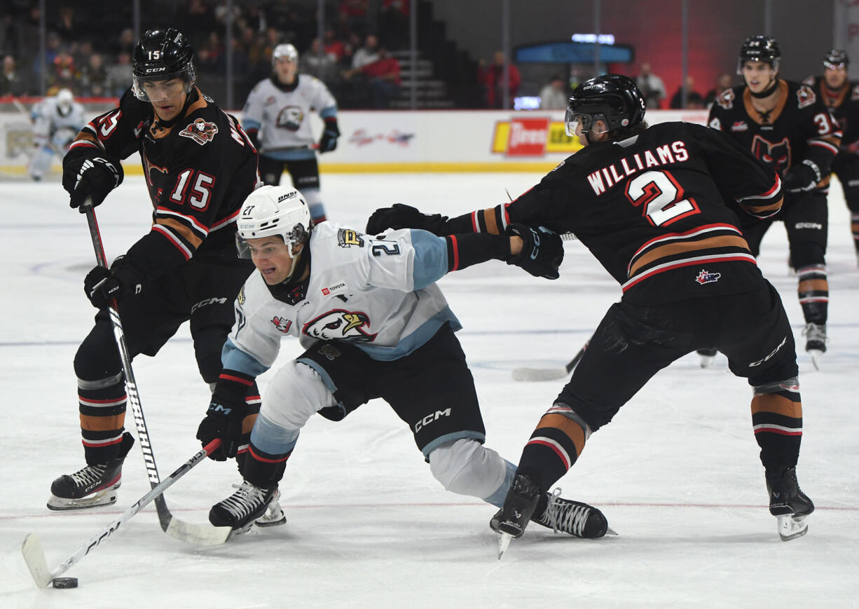 Portland Winterhawks defenseman Tyson Jugnauth (27) chases the puck  between Calgary's Dax Williams (2) and Maxim Muranov (15) during the Western Hockey League game Wednesday, Nov. 13, 2024, at Portland's Veterans Memorial Coliseum.