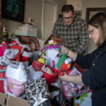 Matt Griffin, left, and Melinda Griffin on Thursday look over gift packages in honor of their daughter, Maddy, pictured at left, who died of brain cancer in 2022. They now honor their daughter with a Facebook page called “Miracle Maddy,” where they advocate for spreading awareness of childhood cancers. Every holiday season, the Griffin family makes goodie baskets for pediatric oncology patients. (Amanda Cowan/The Columbian)