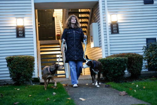 Jessica Poe photographed with her two dogs, Rango (black and white) and Bijou after she comes home from work at her apartment in Redmond, Washington, on Tuesday, Nov. 19, 2024. She moved from Spanaway to Redmond for a job that requires her to work in-person five days a week, but her commute is only 15 minutes instead of four hours and she can bring her dogs to work.