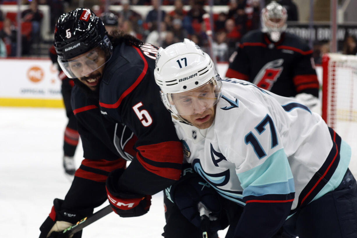 Carolina Hurricanes' Jalen Chatfield (5) battles with Seattle Kraken's Jaden Schwartz (17) for the puck during the first period of an NHL hockey game in Raleigh, N.C., Tuesday, Dec. 3, 2024.