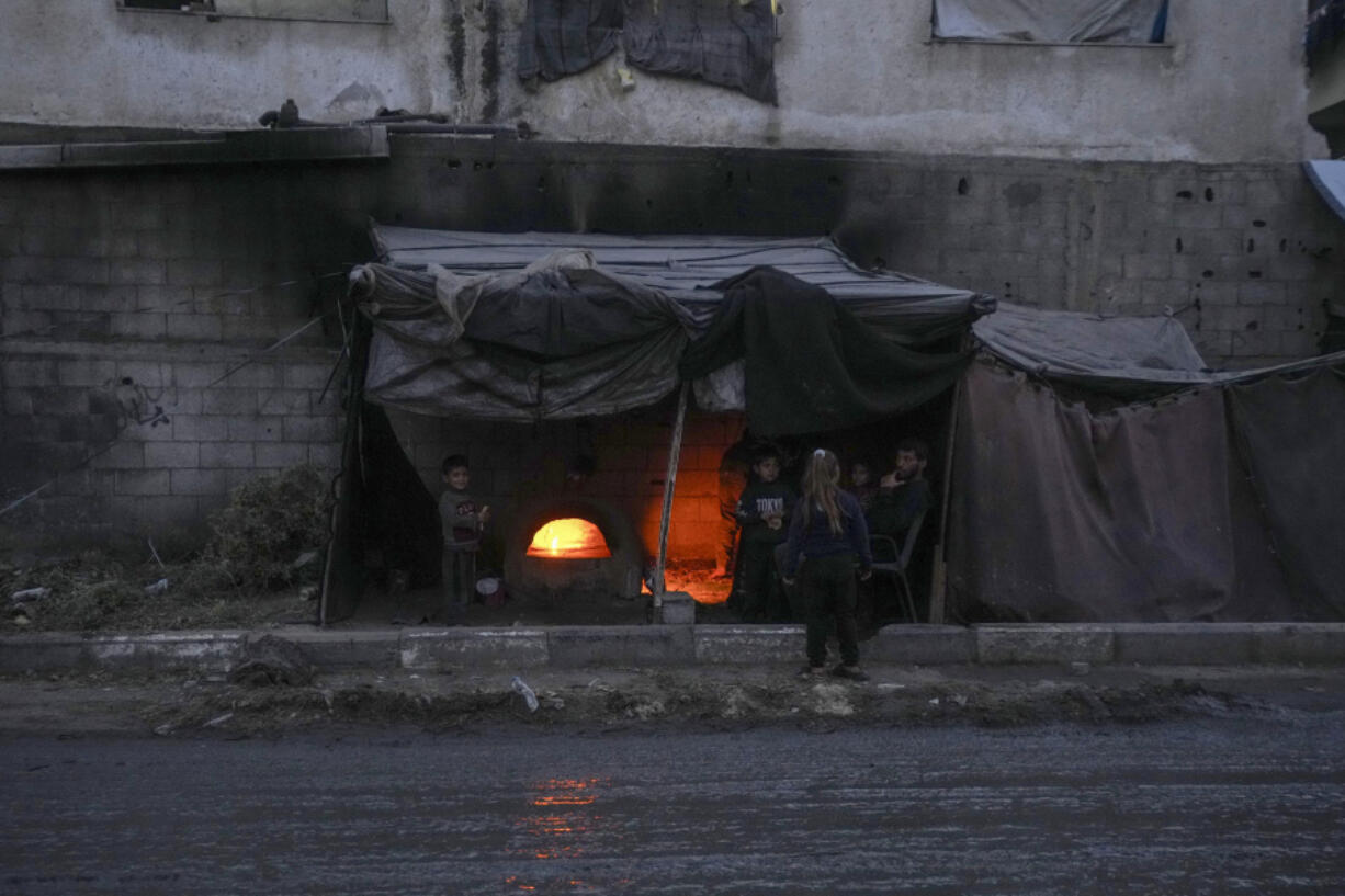 Displaced Palestinians sit next to a makeshift oven on a tent set up on an area in Deir al-Balah, Gaza Strip Thursday, Dec. 5, 2024.