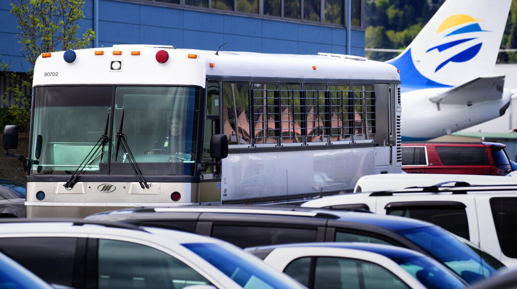 A bus with barred windows carrying detained immigrants from the plane in the background leaves Boeing Field around noon on Tuesday, April, 23, 2019. The charter flight from Phoenix was operated for Immigration and Customs Enforcement (ICE).