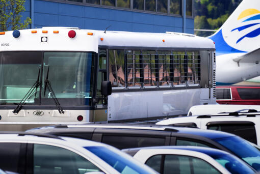 A bus with barred windows carrying detained immigrants from the plane in the background leaves Boeing Field around noon on Tuesday, April, 23, 2019. The charter flight from Phoenix was operated for Immigration and Customs Enforcement (ICE).